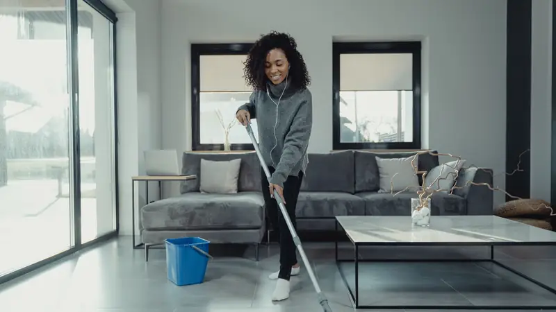 A person mopping the tiled floor of a bright, modern living room with large windows