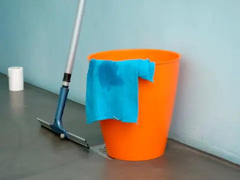 An orange cleaning bucket with a blue cloth and a floor squeegee on a clean floor