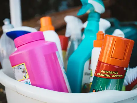 A caddy of cleaning supplies with spray bottles, a brush and cloths