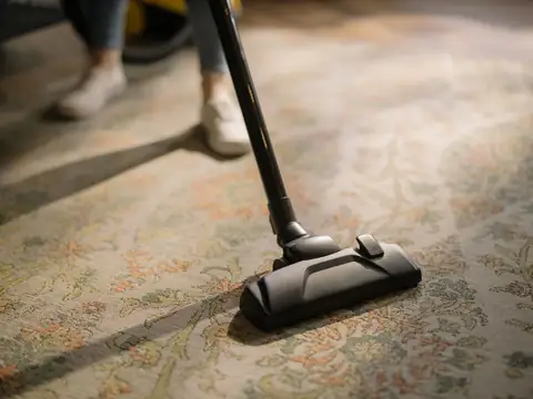 A person vacuuming a patterned rug in a sunlit room